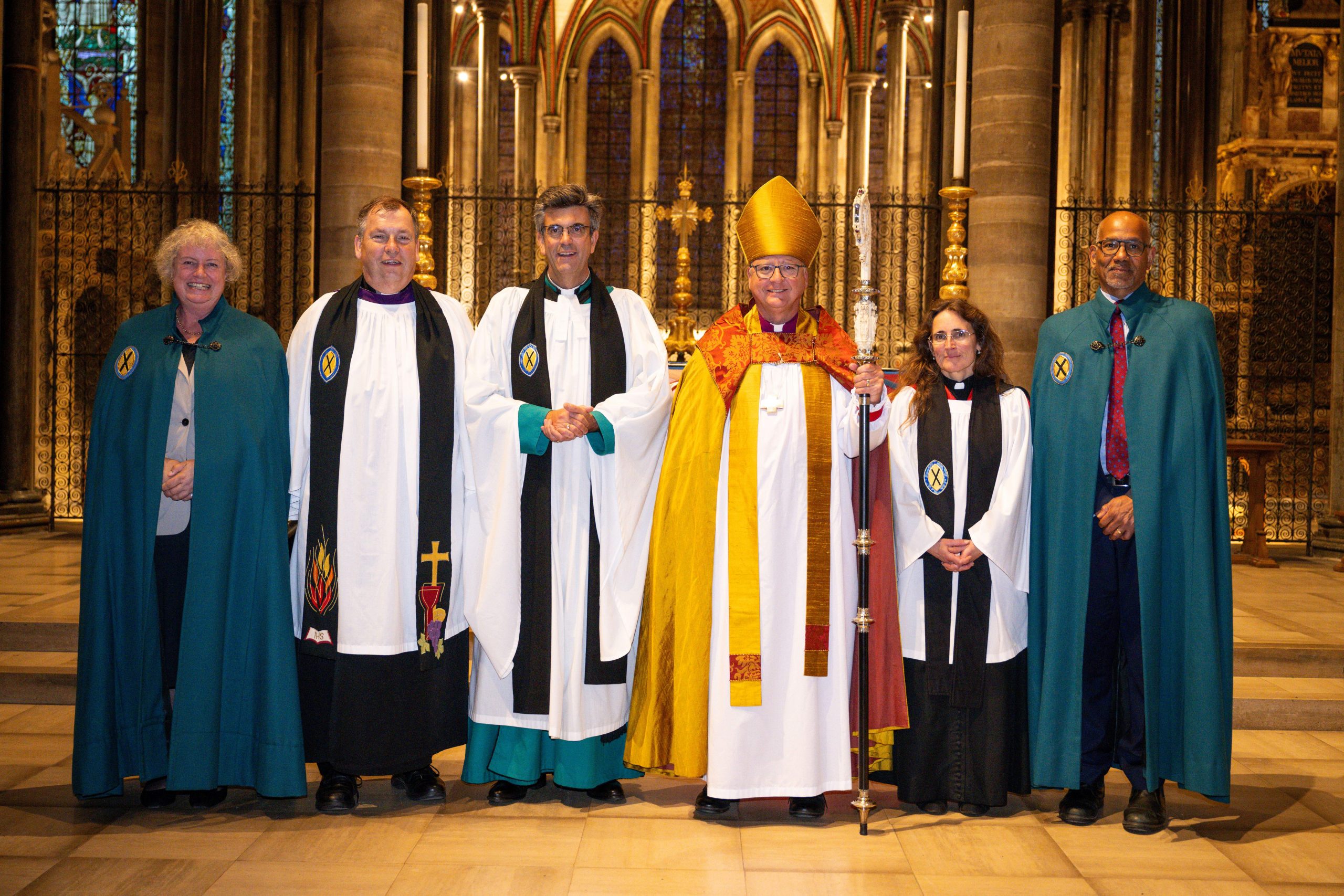 Sue de Candole, the Revd Paul Brooks, The Dean of Salisbury, The Very Revd Nicholas Papadopulos, The Bishop of Salisbury, the Right Revd Stephen Lake, The Revd Kate McFarlane and Alan Smith stand in a line in front of the altar smiling to camera